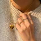 Hand wearing a gold ring with a heart pendant on a textured surface