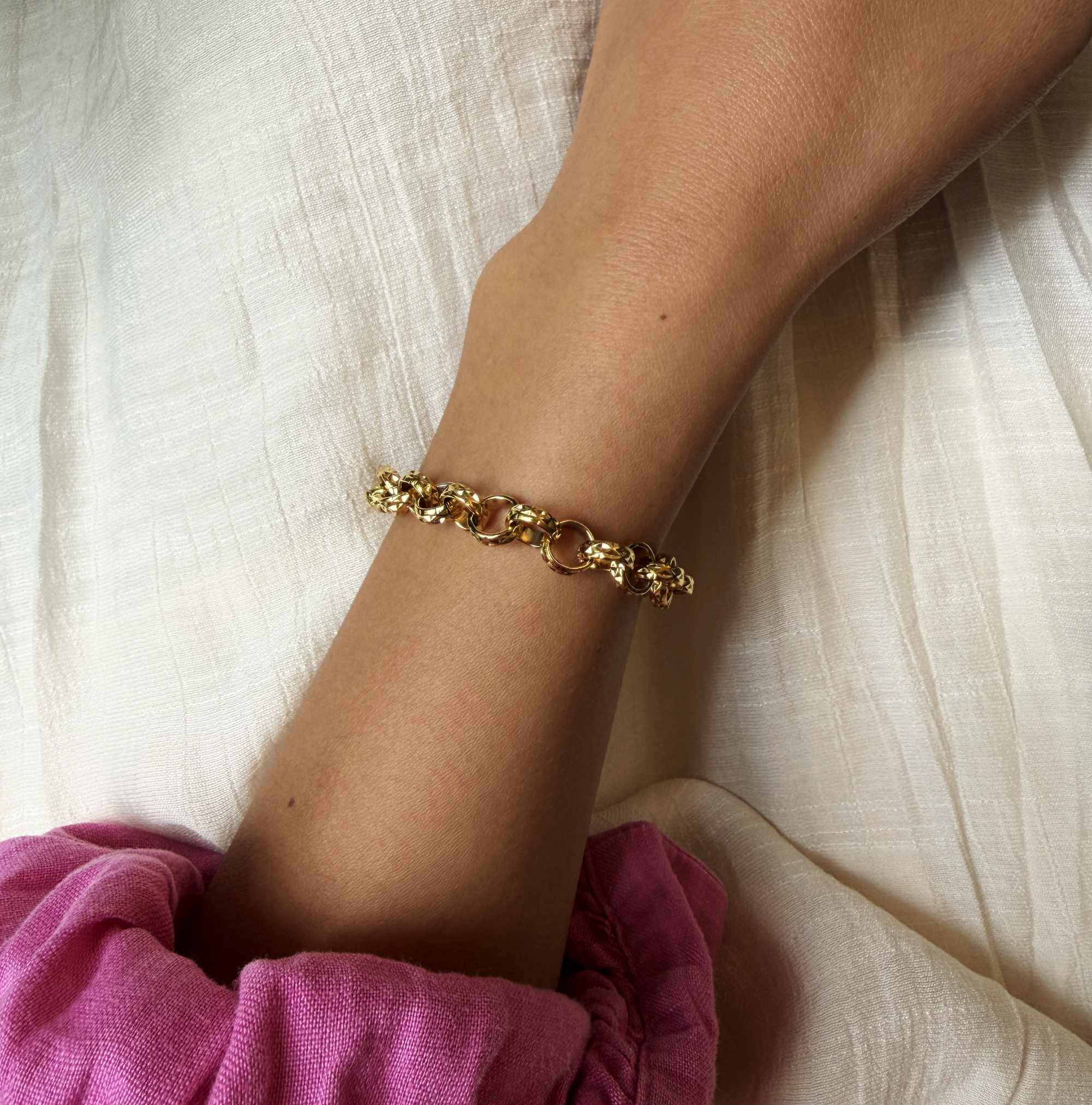 Gold bracelet on a wrist with a white fabric background