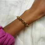 Gold chain bracelet on a wrist with a pink sleeve against a white fabric background