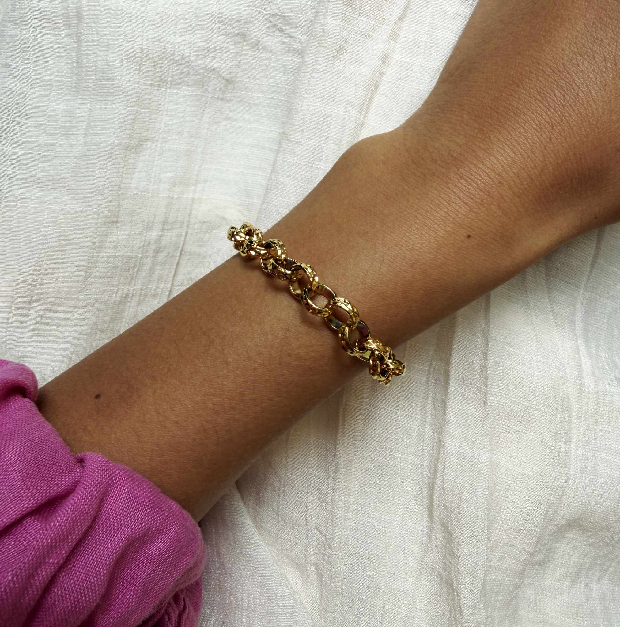 Gold chain bracelet on a wrist with a pink sleeve against a white fabric background