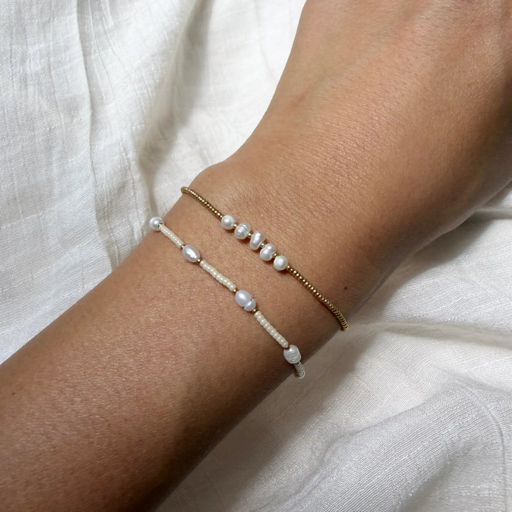 Two pearl bracelets on a wrist against a white fabric background