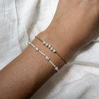 Two pearl bracelets on a wrist against a white fabric background