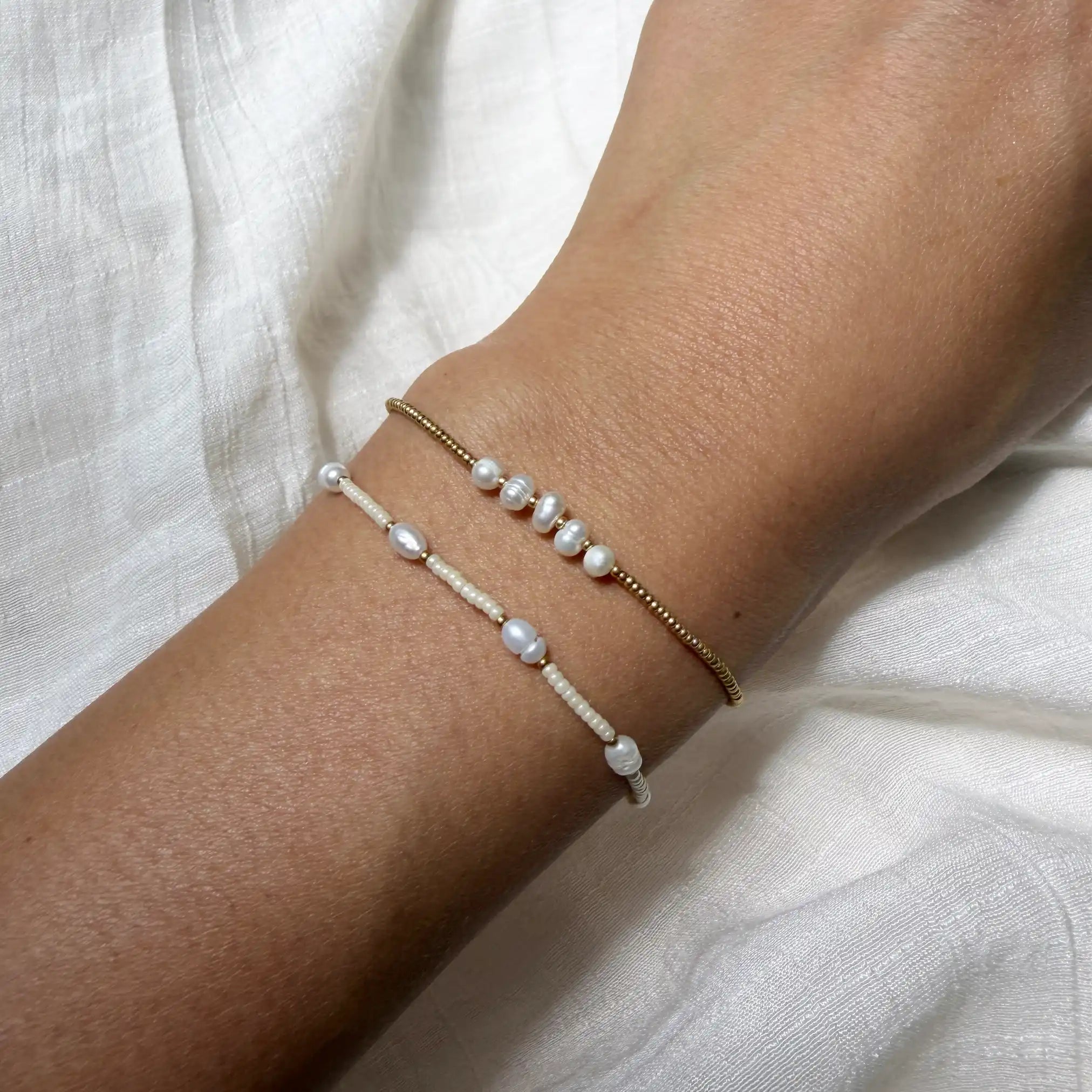 Two pearl bracelets on a wrist against a white fabric background