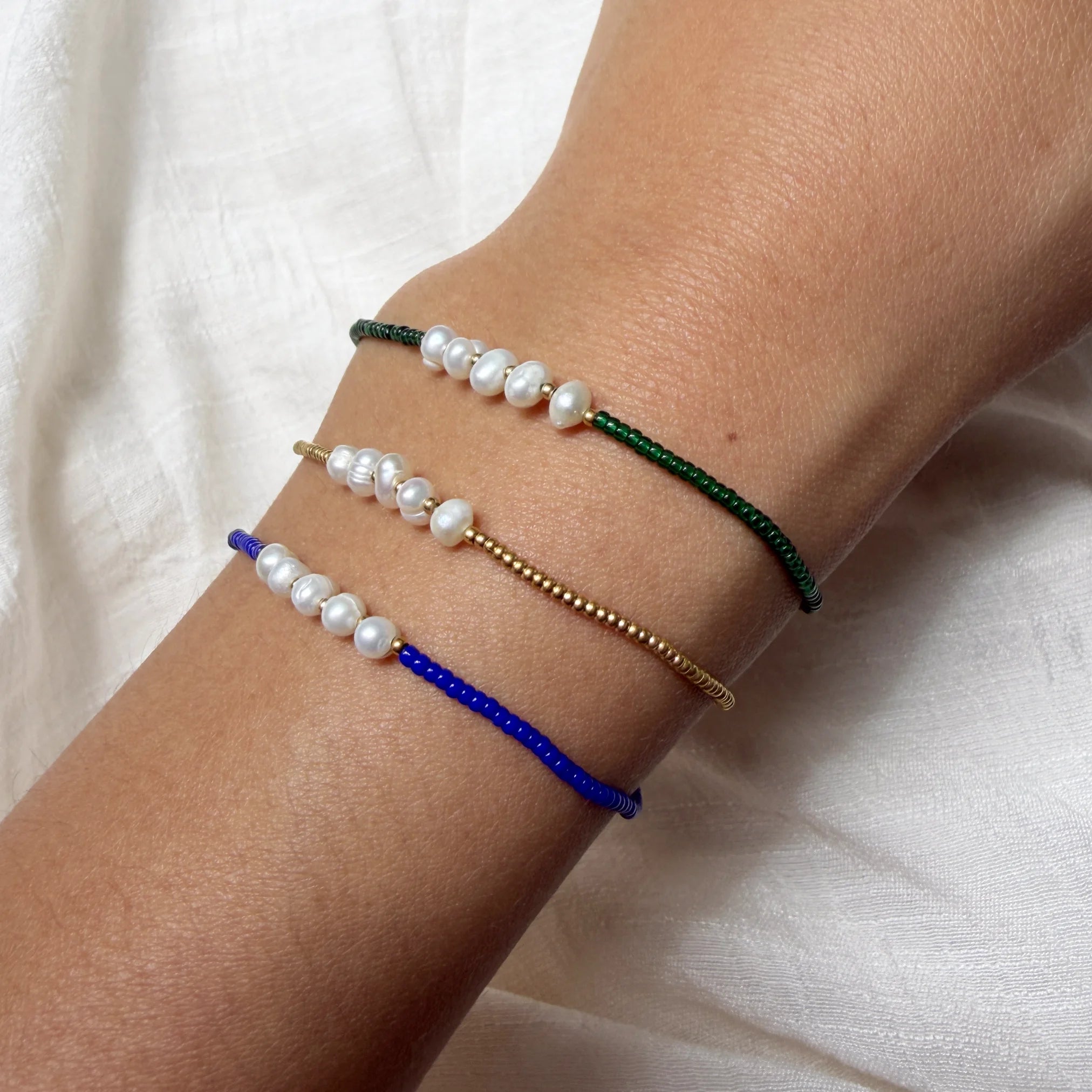 Three pearl bracelets on a wrist against a white background