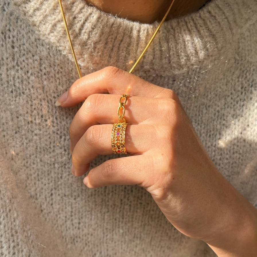 Hand wearing a gold ring with a matching necklace against a neutral background
