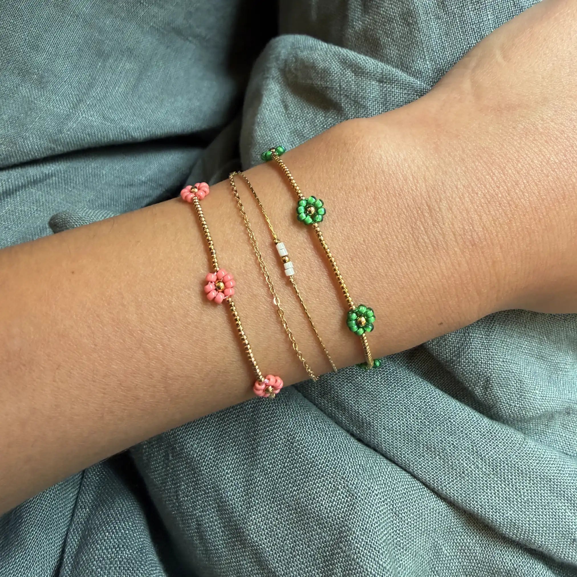 Close-up of a wrist wearing multiple floral bracelets on a green fabric background