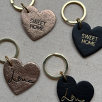 Heart-shaped keychains with 'Sweet Home' and 'Love' text on a textured surface