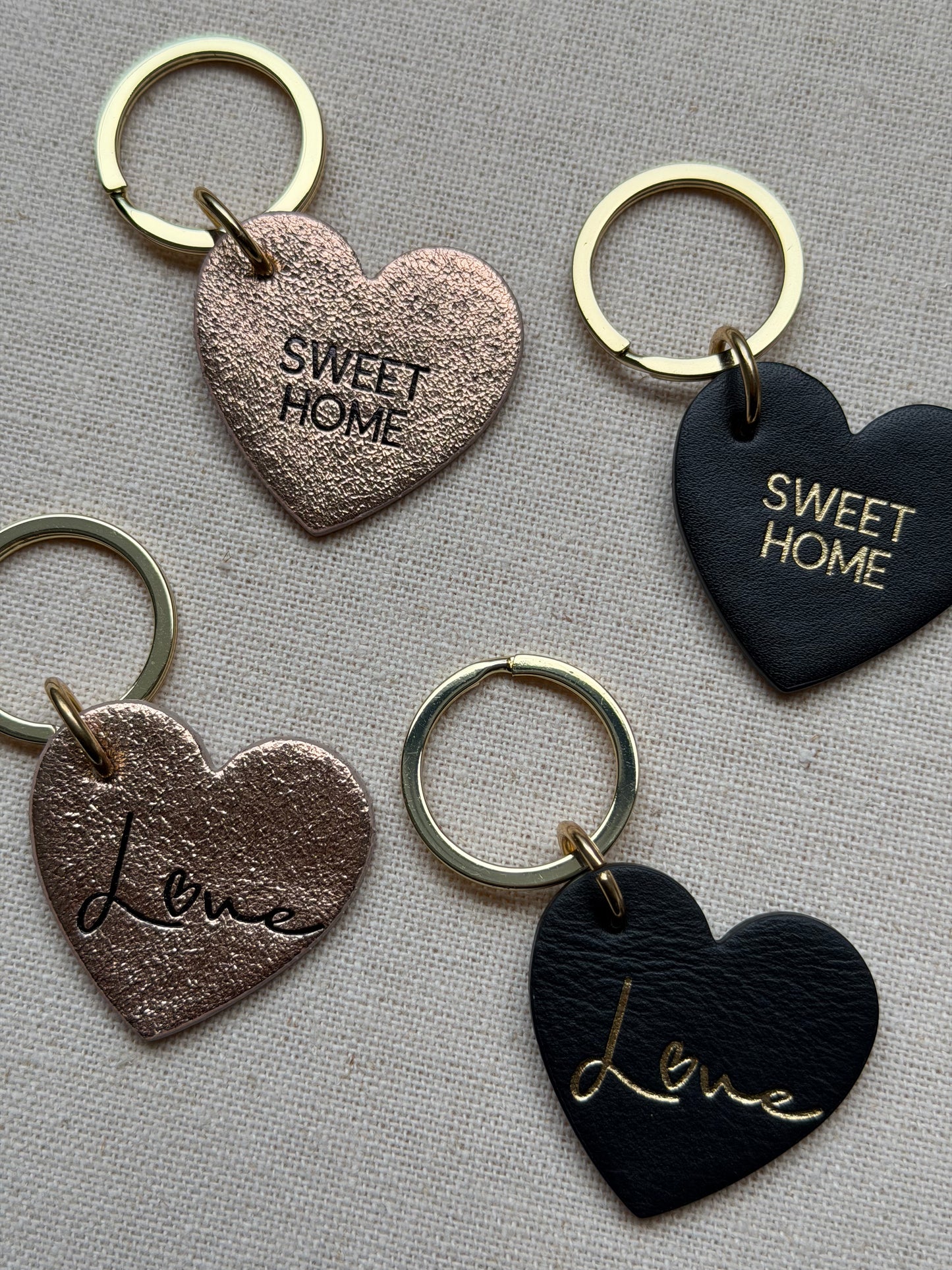 Heart-shaped keychains with 'Sweet Home' and 'Love' text on a textured surface