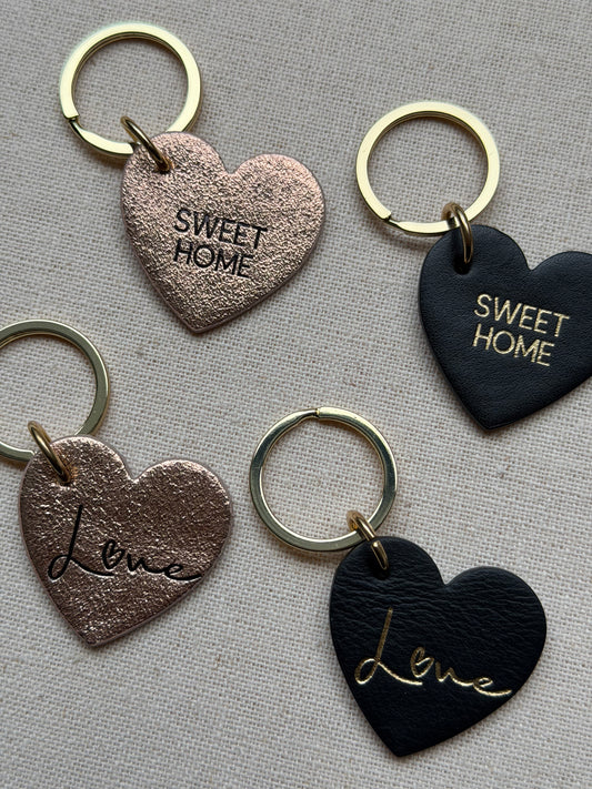 Heart-shaped keychains with 'Sweet Home' and 'Love' text on a textured surface