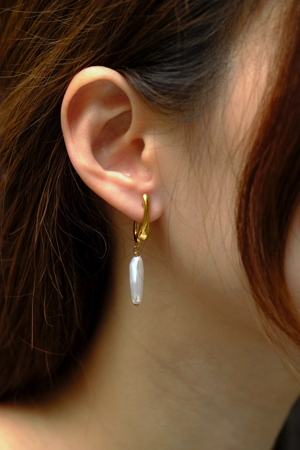 Close-up of an ear wearing a gold hoop earring with a pearl drop.