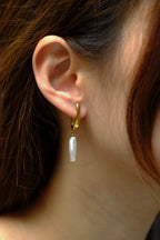 Close-up of an ear wearing a gold hoop earring with a pearl drop.
