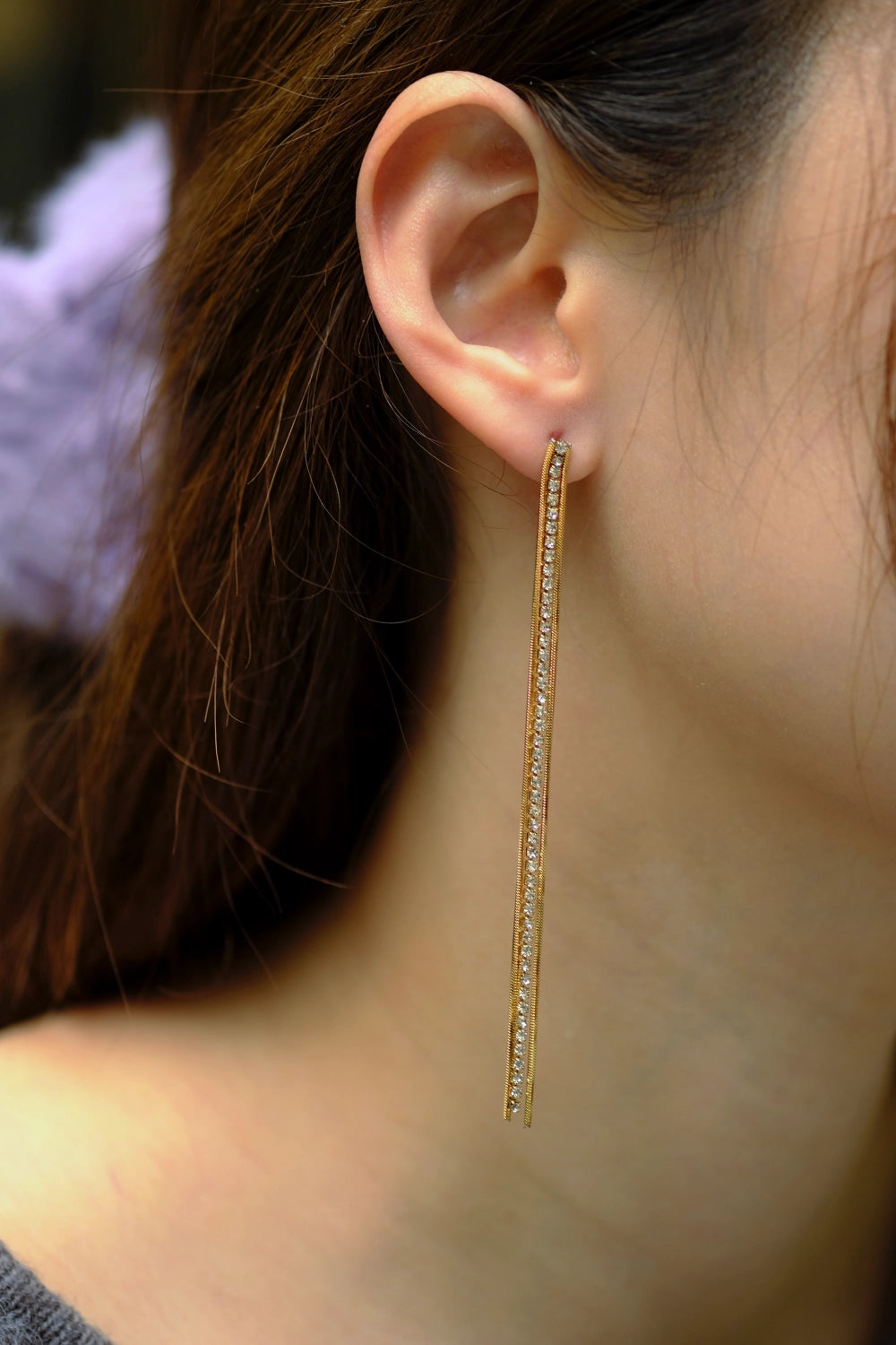 Long gold earring worn by a person with blurred background