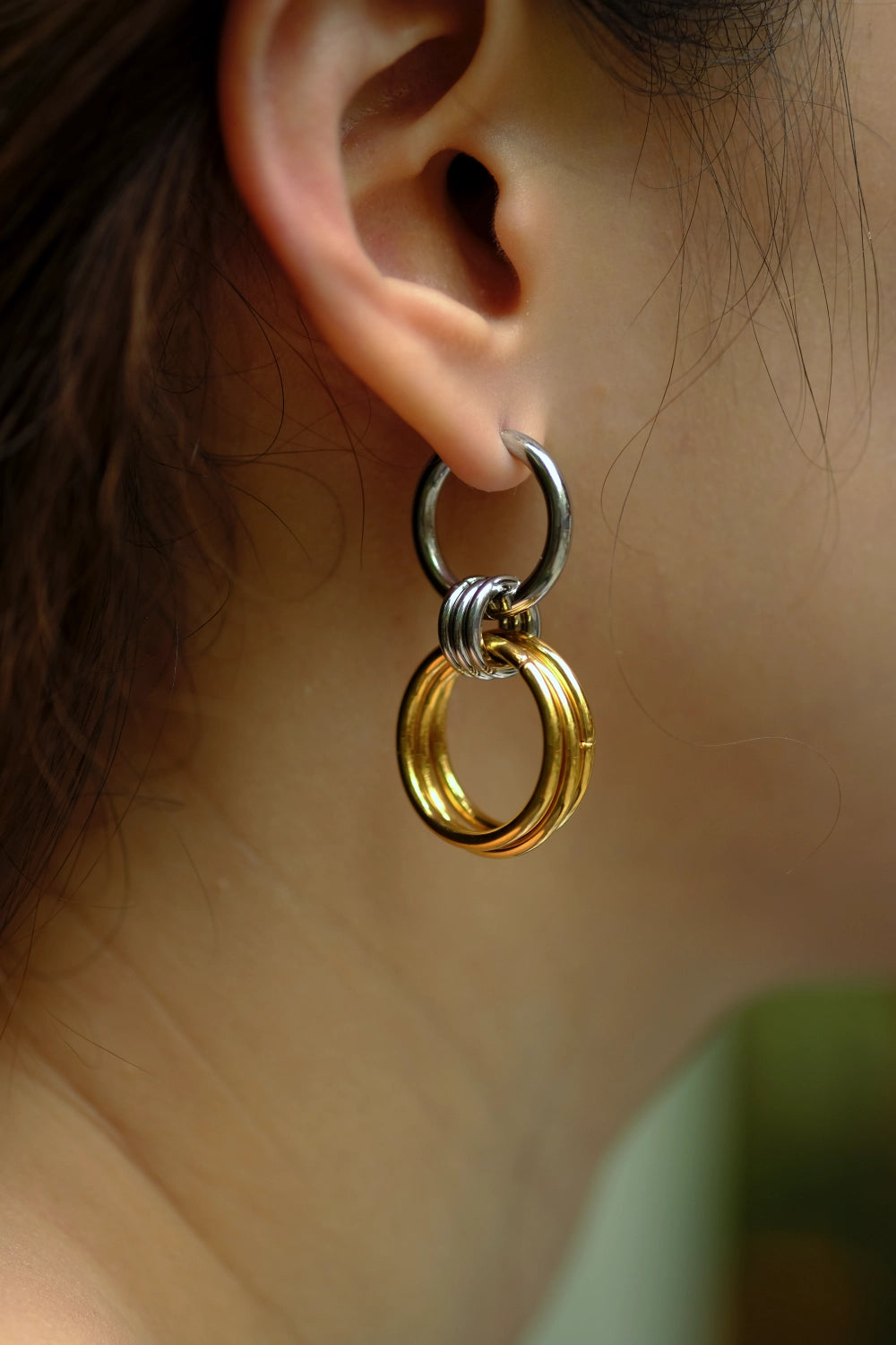 Close-up of a gold and silver earring worn on an ear with a blurred background