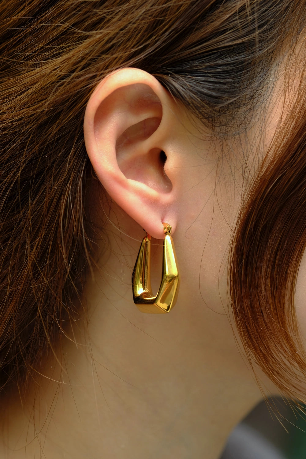 Gold hoop earring worn by a person with brown hair.