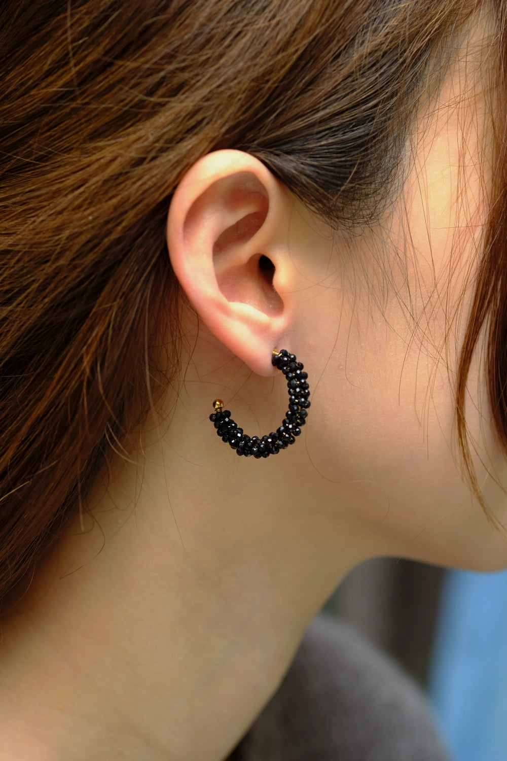 Close-up of an ear wearing a black beaded hoop earring with blurred background