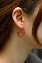 Close-up of an ear wearing a red beaded hoop earring with blurred background