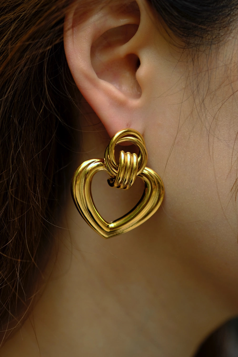 Gold heart-shaped earring worn on an ear with a blurred background
