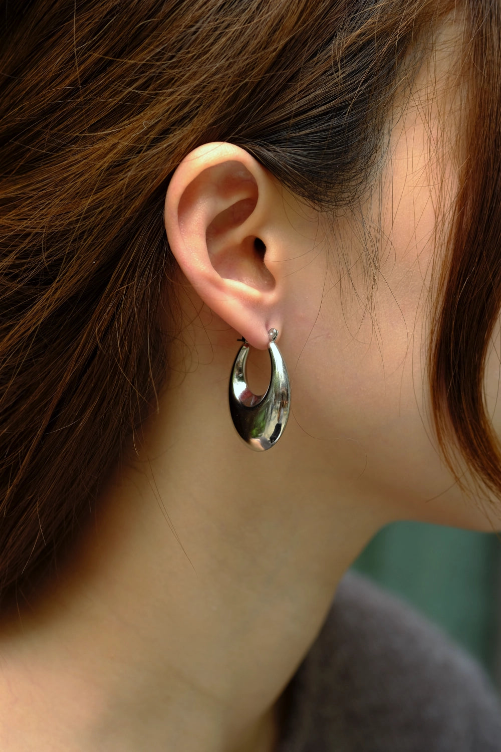 Close-up of a person wearing a silver hoop earring with blurred background