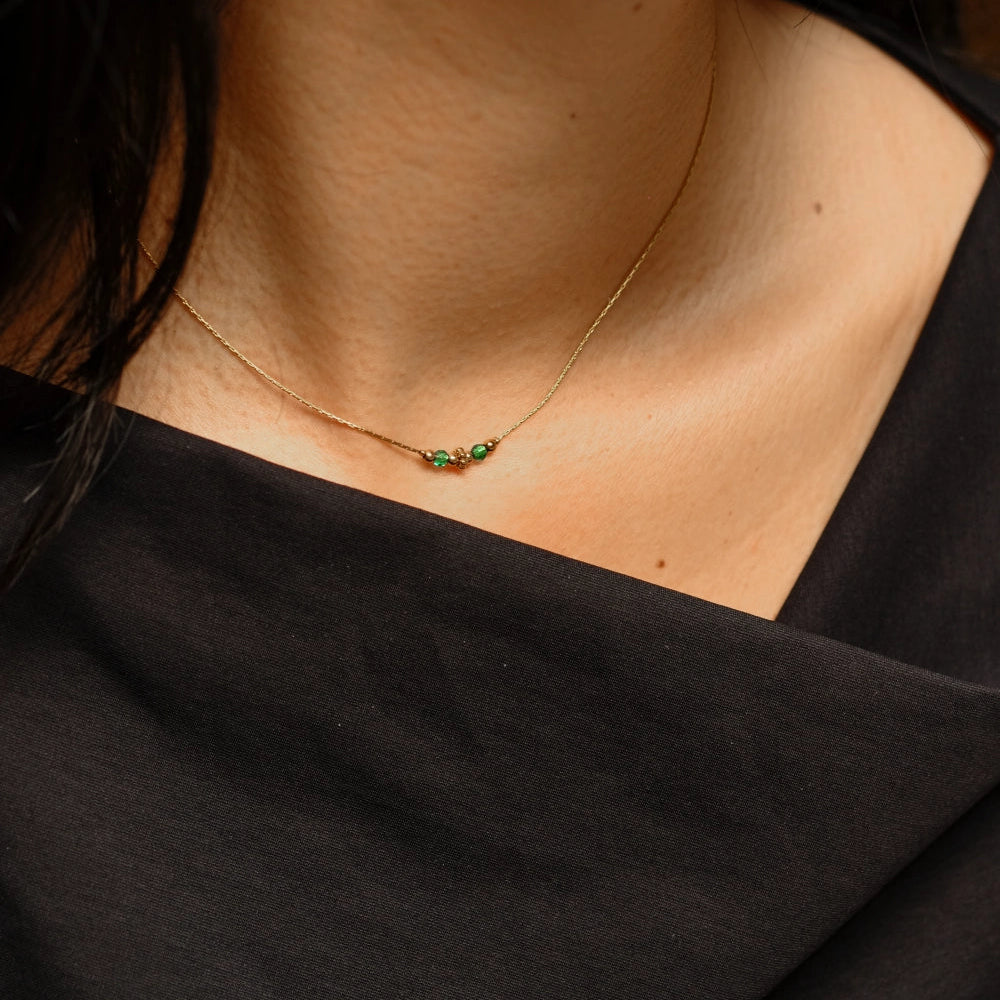 Necklace with green gemstones worn by a person against a black background