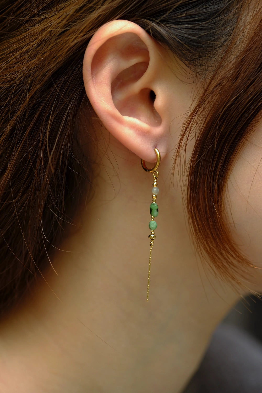 Close-up of an ear wearing a gold earring with green beads.
