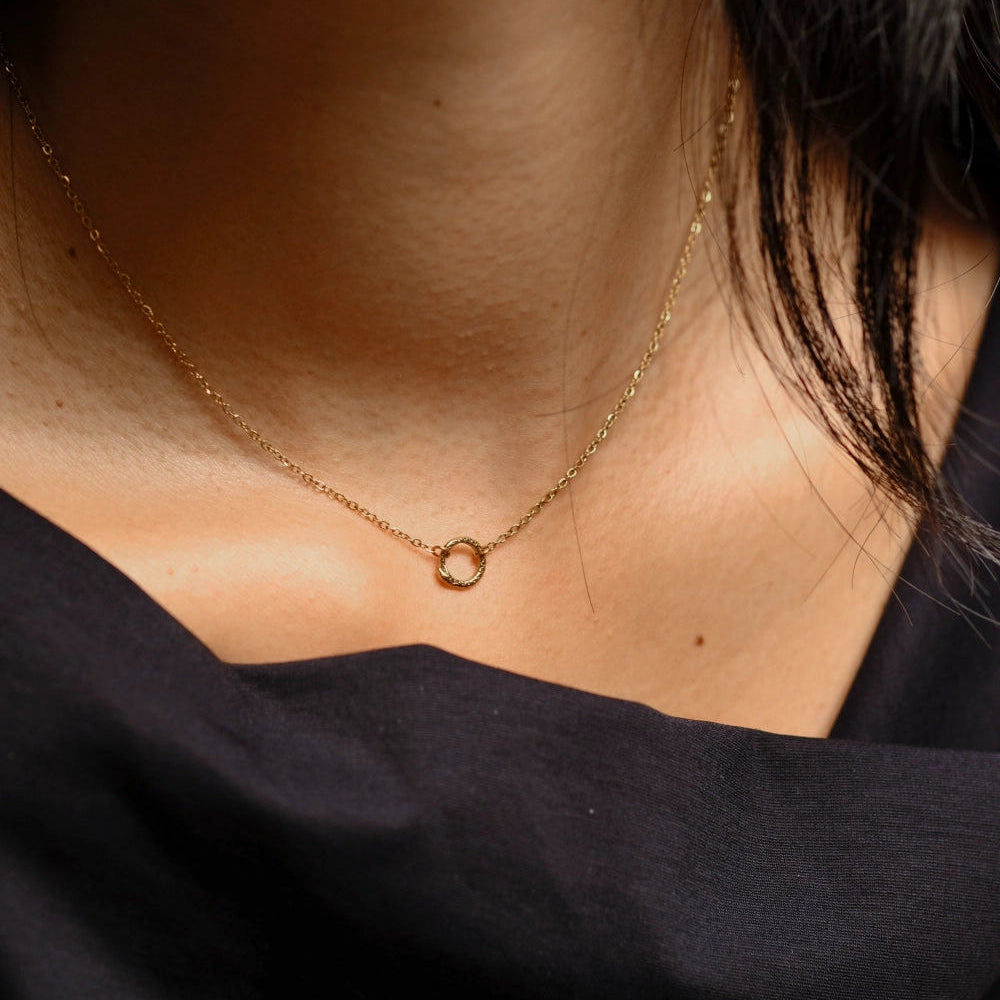 Close-up of a person wearing a delicate gold necklace against a black background