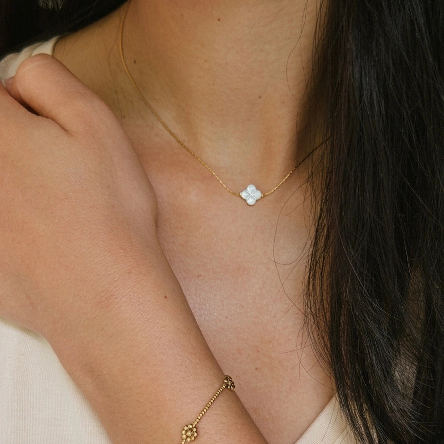 Close-up of a person wearing a gold necklace and bracelet on a plain background