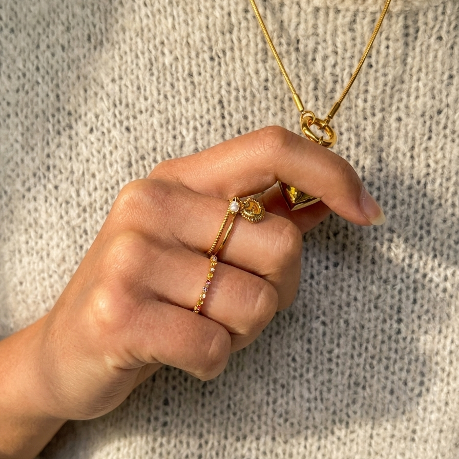 Hand wearing gold jewelry on a textured beige background