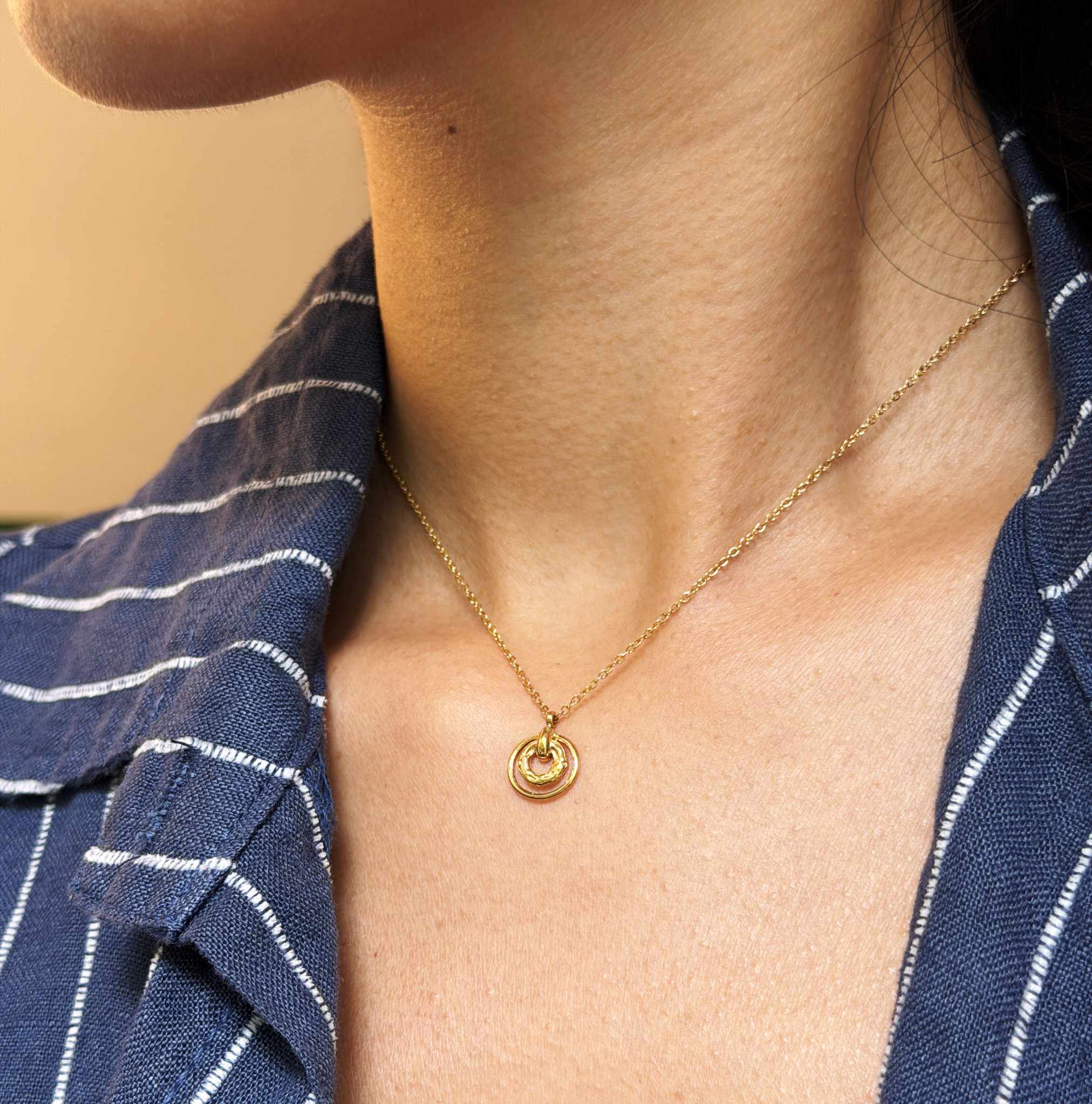 Gold necklace with a pendant worn by a person in a blue striped shirt.