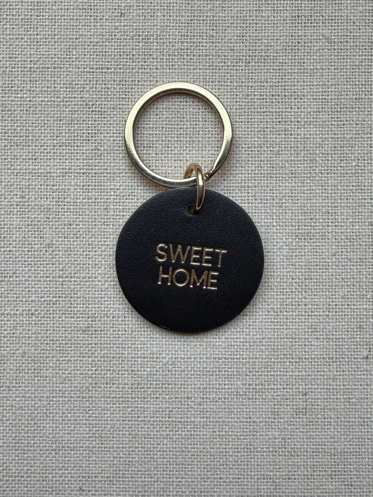 black Keychain with 'Sweet Home' tag on a gray fabric background
