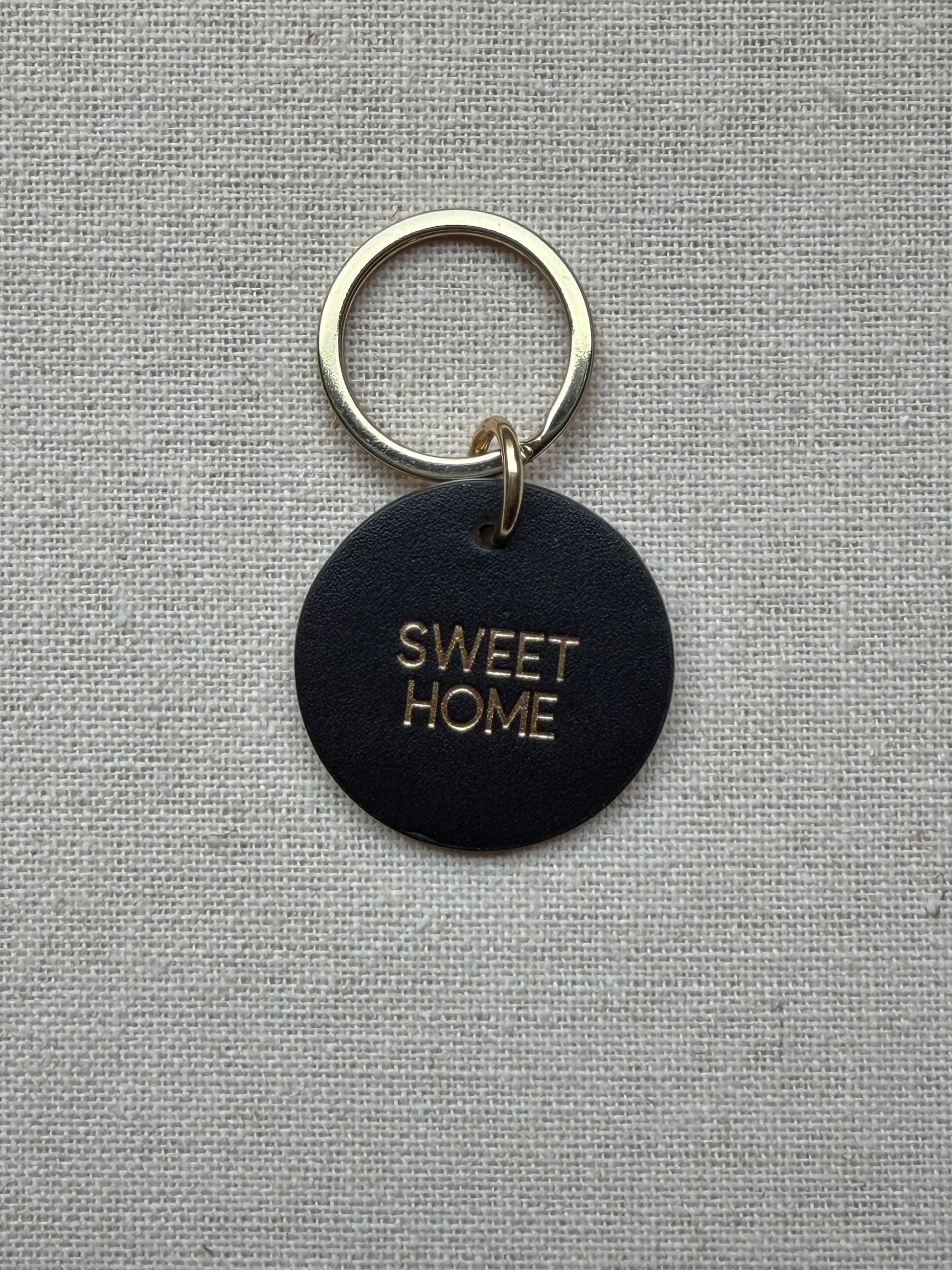 black Keychain with 'Sweet Home' tag on a gray fabric background