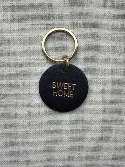 black Keychain with 'Sweet Home' tag on a gray fabric background