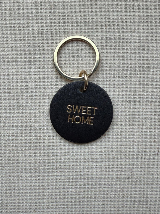 black Keychain with 'Sweet Home' tag on a gray fabric background