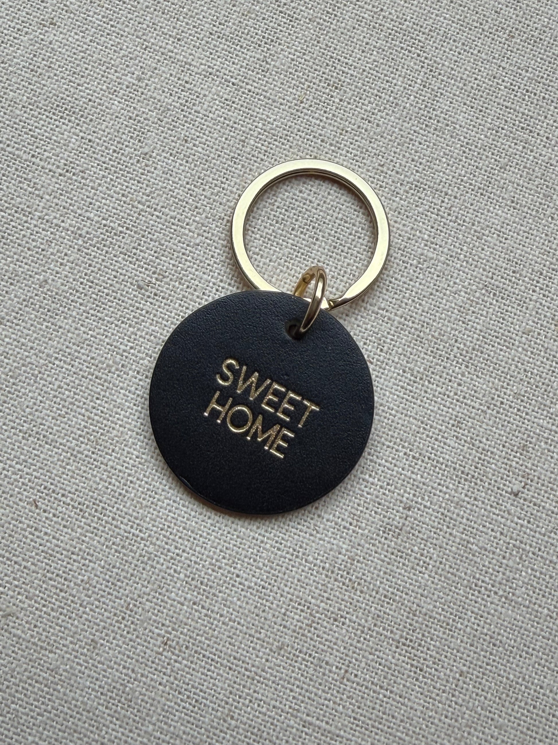 Black keychain with 'SWEET HOME' text on a gray fabric background