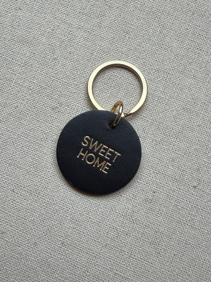 Black keychain with 'SWEET HOME' text on a gray fabric background