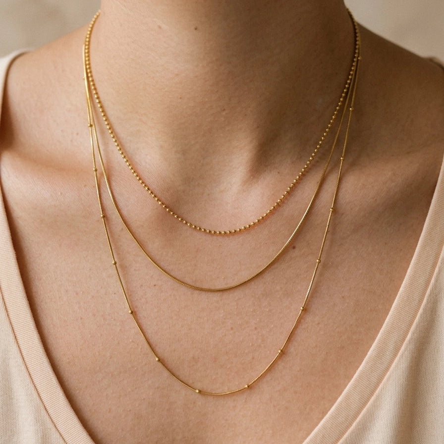 Close-up of a person wearing two gold necklaces on a neutral background