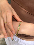A close-up of a person's wrist wearing a gold bangle bracelet with green and yellow stones, alongside a matching gold ring on their finger.