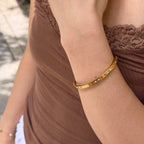 A close-up of a woman's wrist wearing a thin gold bangle bracelet with small clear stones, paired with a brown lace-trim top.