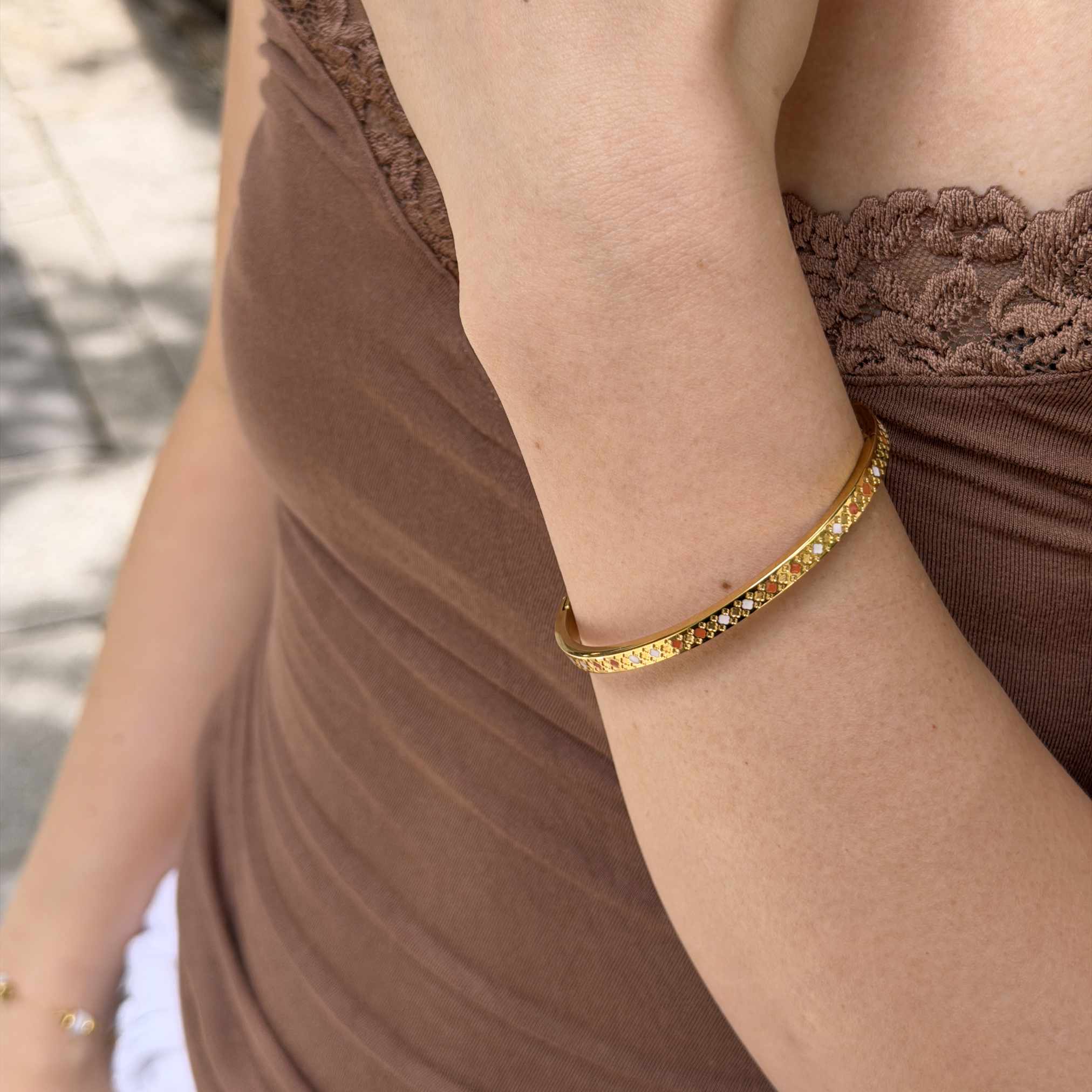 A close-up of a woman's wrist wearing a thin gold bangle bracelet with small clear stones, paired with a brown lace-trim top.