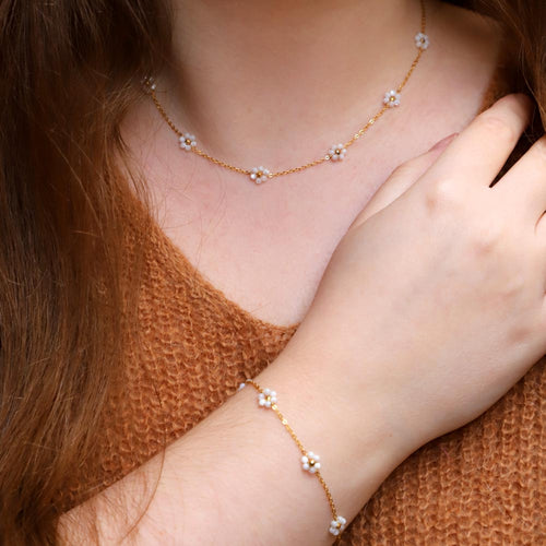 A person wearing a stainless steel necklace with gold plating and small white gemstones, paired with a matching bracelet.
